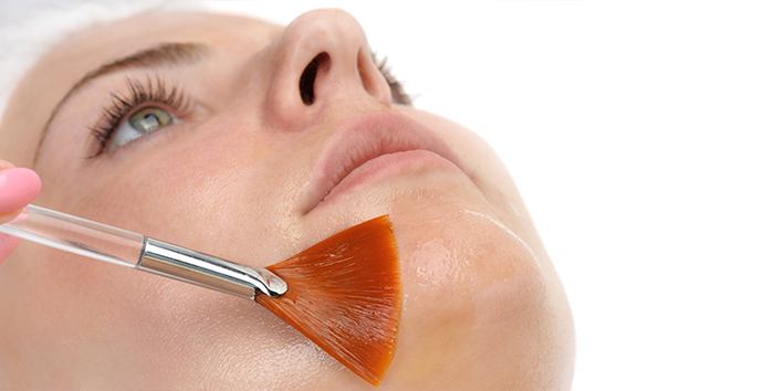 Esthetician applying a chemical peel solution to a patient's cheek with a brush